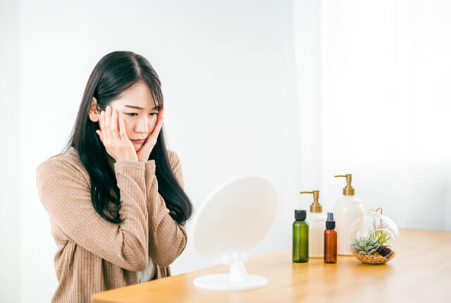 頬に手を当てて鏡を見ている女性